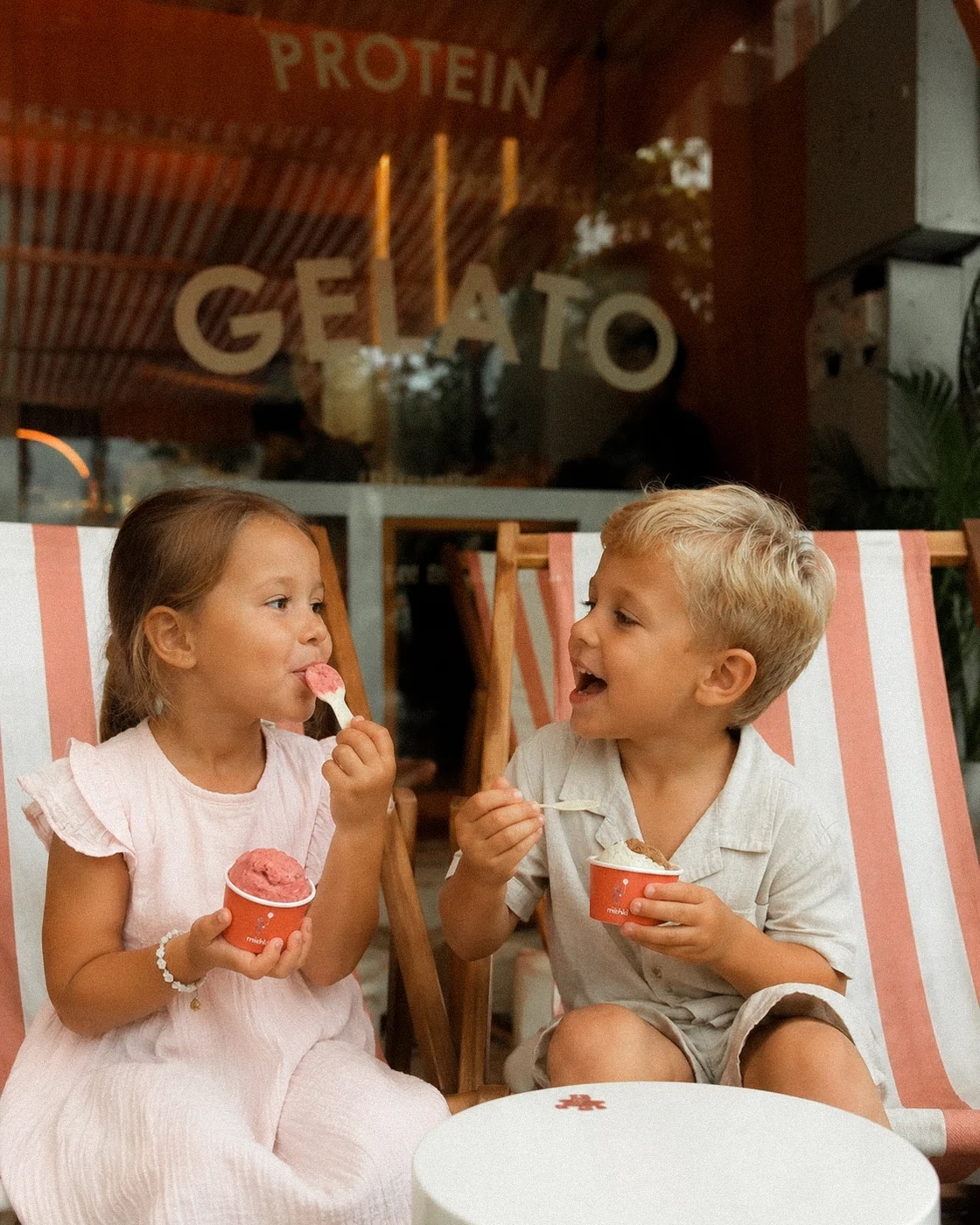 Two children eating Mishki gelato on striped deck chairs outside the shop